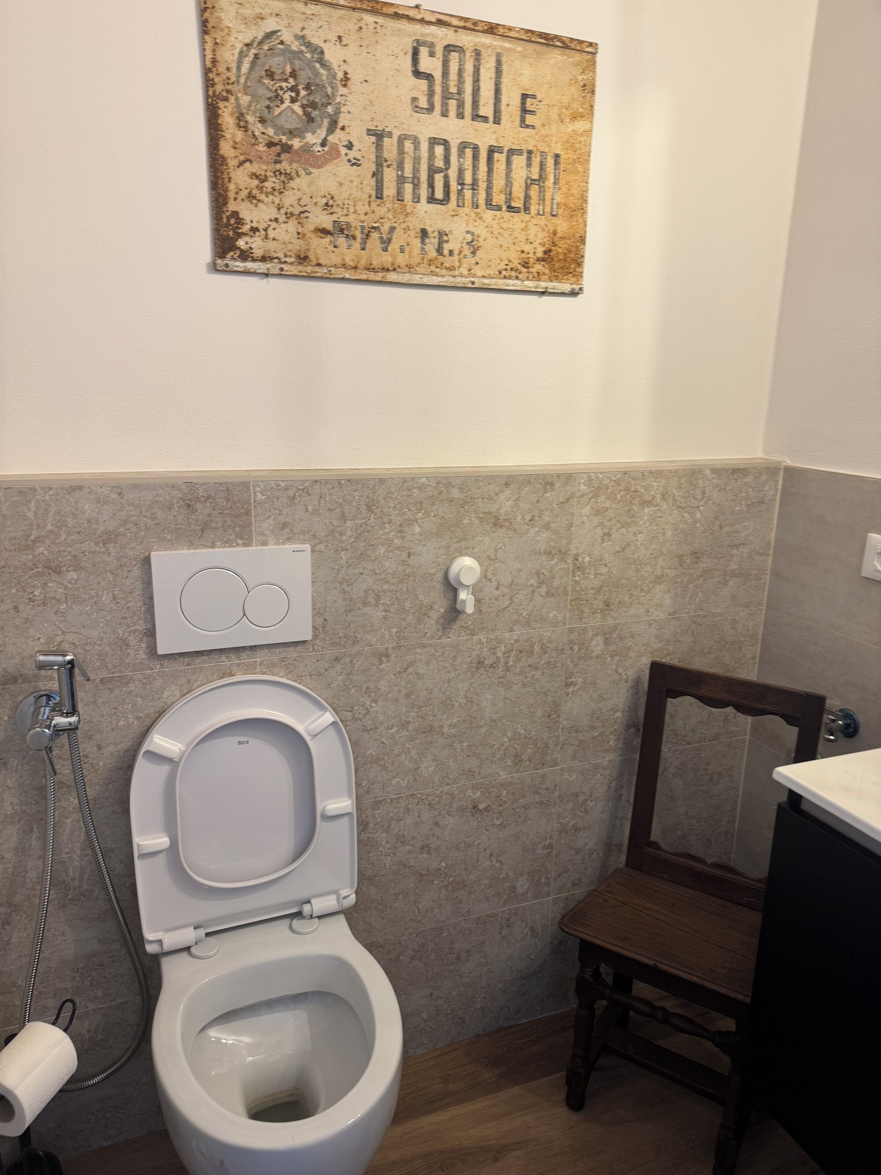 Une salle de bain avec des toilettes, une douche, une chaise en bois et un panneau sur le mur.