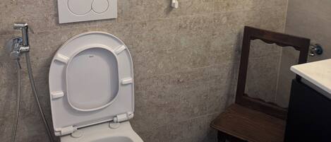 Une salle de bain avec des toilettes, une douche, une chaise en bois et un panneau sur le mur.