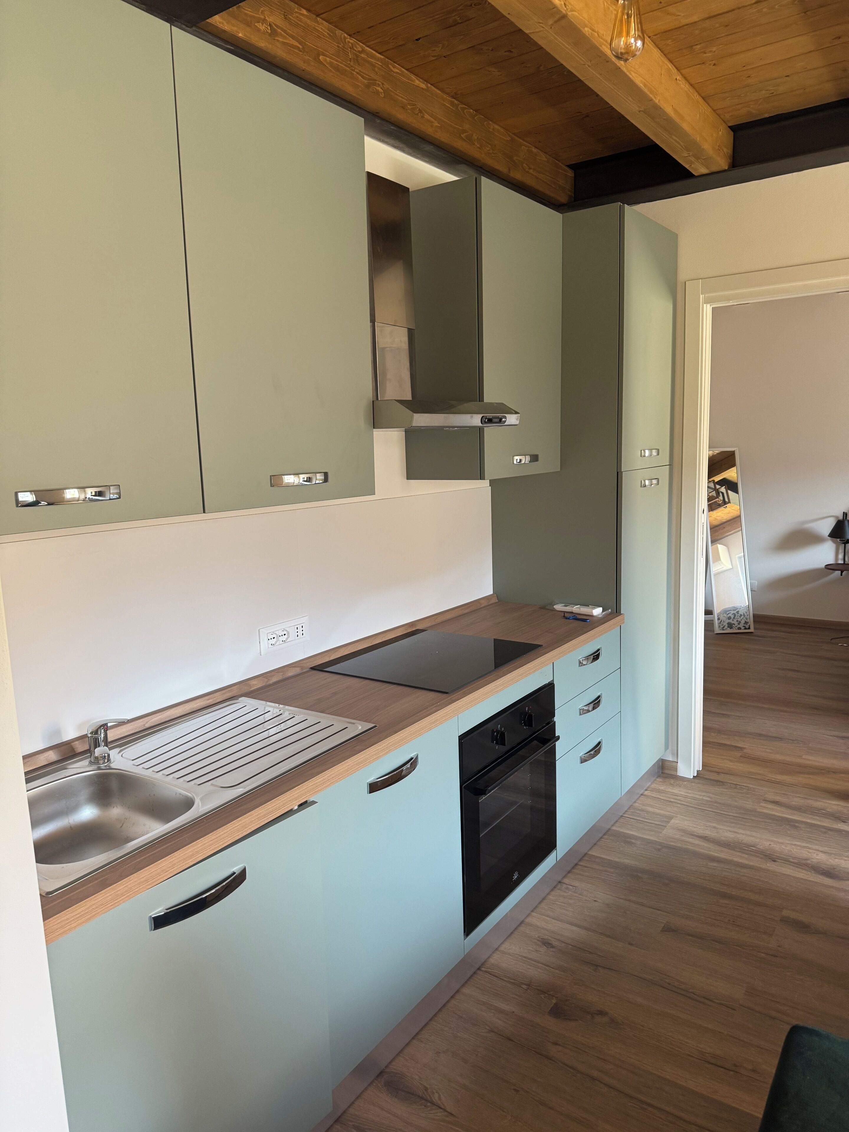 Eine moderne Küche mit hellblauen Schränken, einer Holz Arbeitsplatte, einer Edelstahl-Spüle und einem schwarzen Backofen.