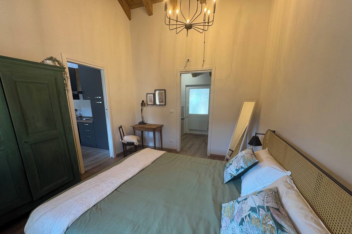 A bedroom with a bed, a desk, a chair, and a door leading to another room.