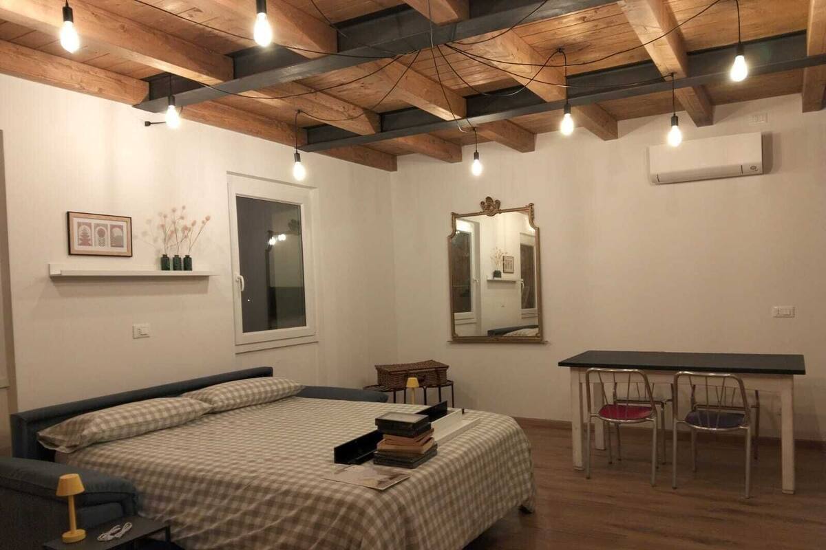 A bedroom with a bed, bedside table, lamp, mirror, and a desk with chairs.