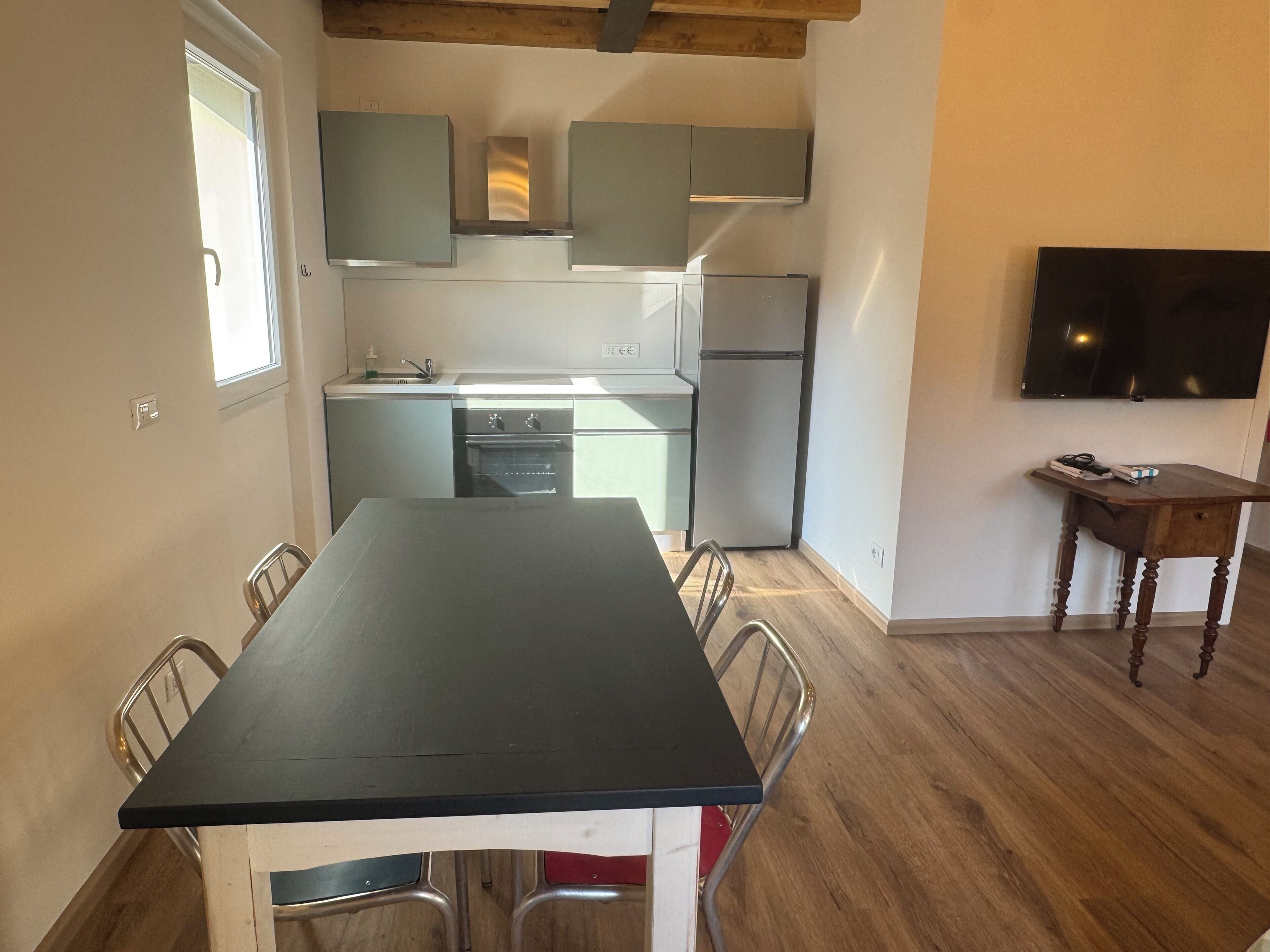 Una cocina compacta con una mesa de comedor, sillas, un refrigerador y un televisor montado en la pared.