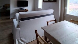 Una habitación con techo de madera, un sofá, un televisor, una mesa de comedor y una ventana.