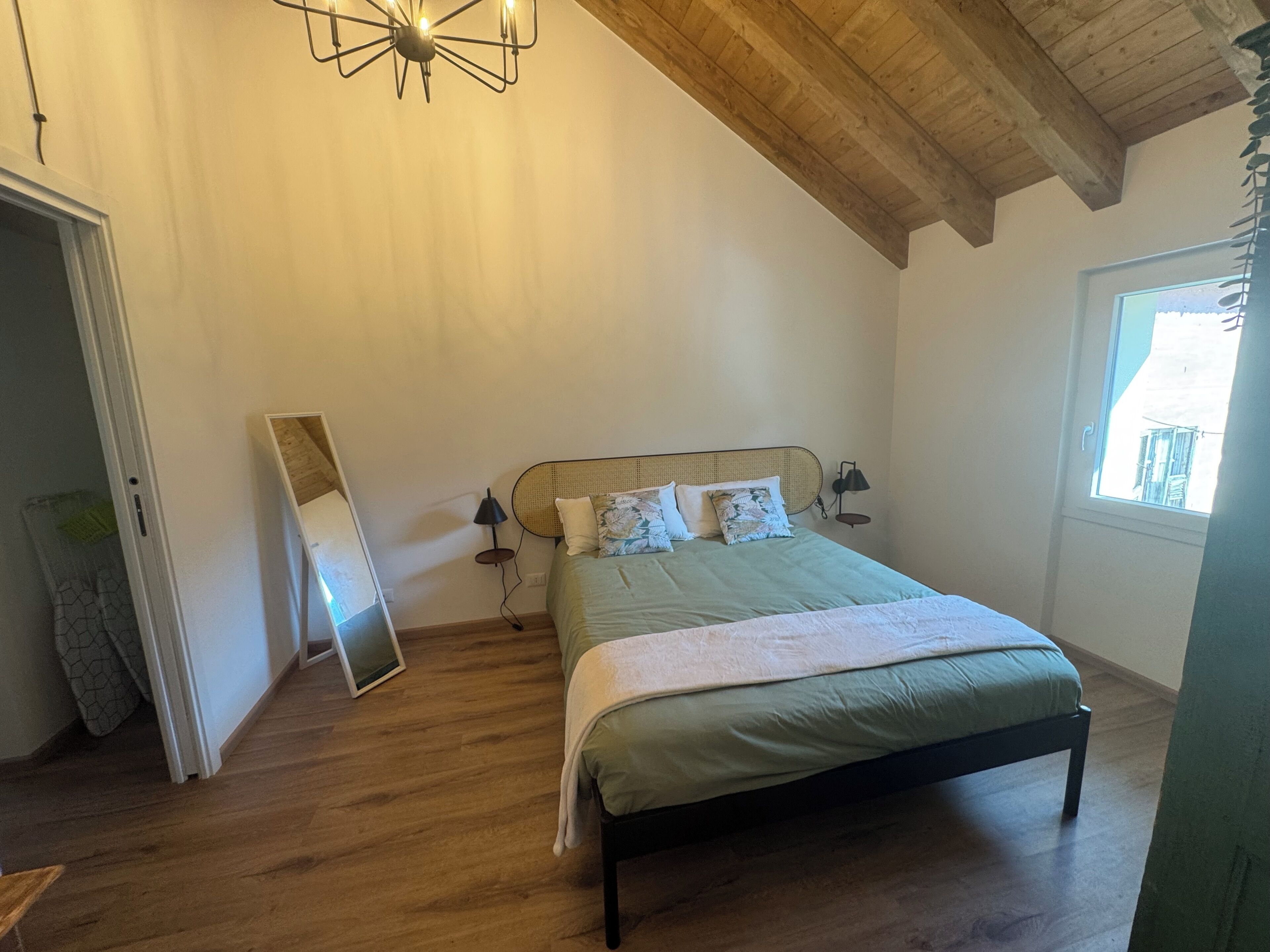 Een slaapkamer met een bed, een houten plafond, een raam en een deur.