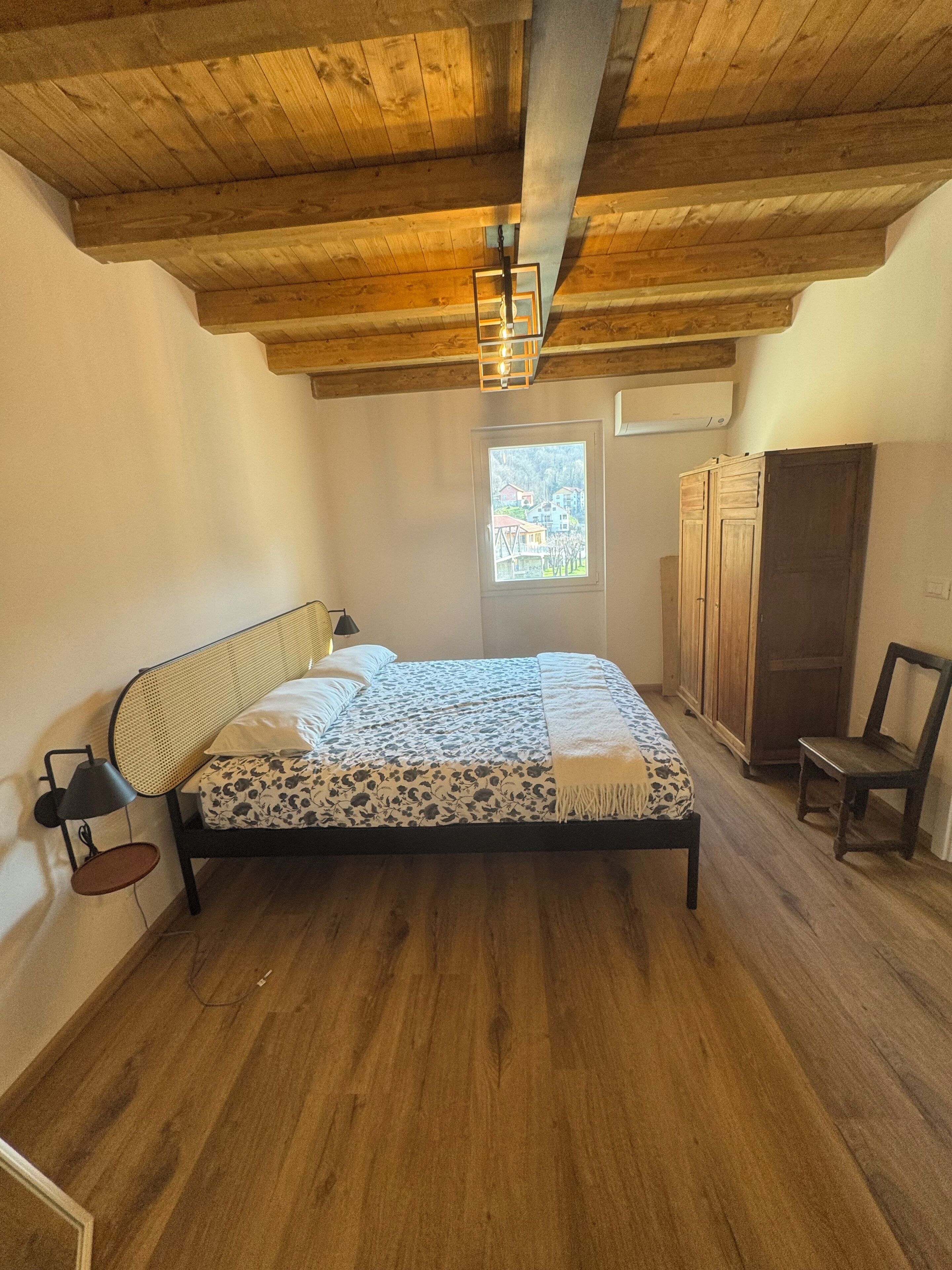 Un dormitorio con techo de madera, una cama con colcha estampada, una ventana con vistas y un armario.