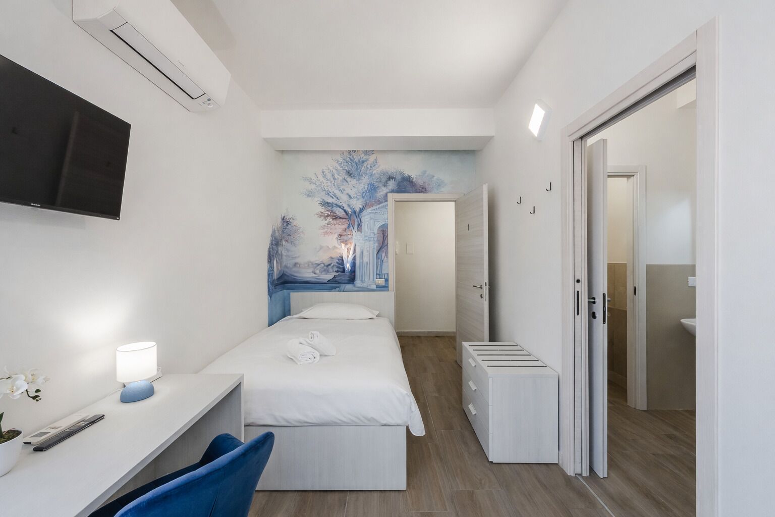A hotel room with a bed, a desk, a chair, a TV, and a painting on the wall.