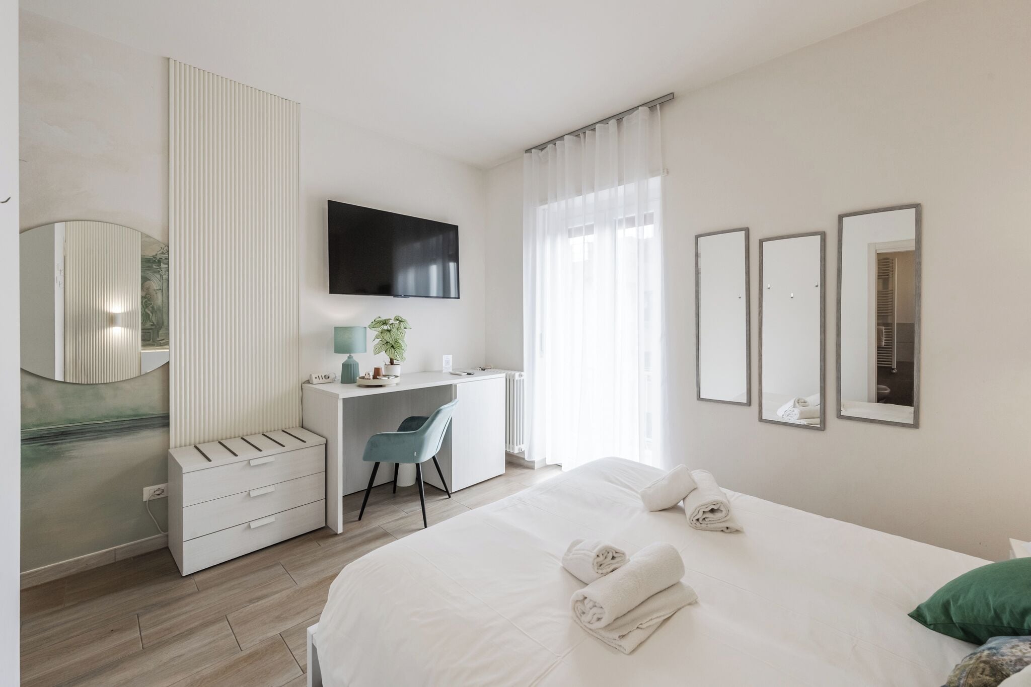 Habitación de hotel con cama, escritorio, silla, televisor y espejo.