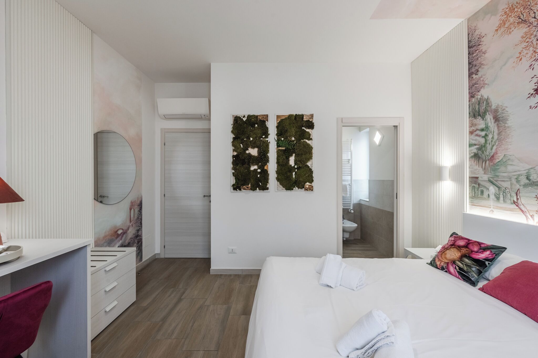Un dormitorio con cama, escritorio, silla, espejo y un pared con dos obras de arte verdes.