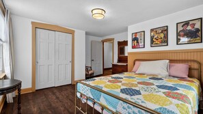 A bedroom with a bed, a dresser, a chair, and a door. There are three posters on the wall. - Victory View 3 Bedroom Home (Gettysburg)
