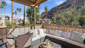 A covered outdoor seating area with a sofa and chairs, overlooking a mountainous landscape with palm trees. - Desert Escape With Private Balcony Condo (Indian Wells)