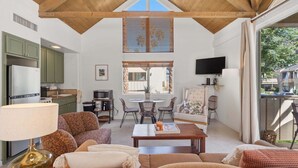 A spacious living area with a high ceiling, a dining table with chairs, a sofa, and a TV mounted on the wall. - Desert Escape With Private Balcony Condo (Indian Wells)