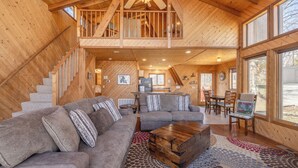 A spacious cabin interior with a loft bedroom, a living area with a sofa and coffee table, and a dining area with chairs and a table. - Grendel Getaway by Innsbrook Vacations! (Innsbrook)