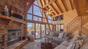 A spacious living room with a stone fireplace, a large window, and a wooden ceiling. - Grendel Getaway by Innsbrook Vacations! (Innsbrook)