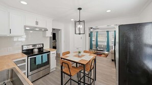 A modern kitchen with white cabinets, a stainless steel stove, and a dining area with a table and chairs. - Peaceful Stay Near Wake Forest 2 Bedroom Home (Franklinton)