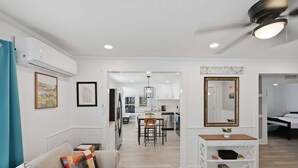 A modern living room with a sofa, a coffee table, and a dining area with chairs and a table. There is a kitchen in the background with cabinets and a countertop. - Peaceful Stay Near Wake Forest 2 Bedroom Home (Franklinton)