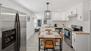 A modern kitchen with stainless steel appliances, white cabinetry, and a wooden dining table. - Peaceful Stay Near Wake Forest 2 Bedroom Home (Franklinton)
