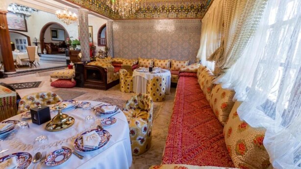 Un interior lujoso con decoración elaborada, un papel tapiz estampado y una zona de estar con alfombra roja.