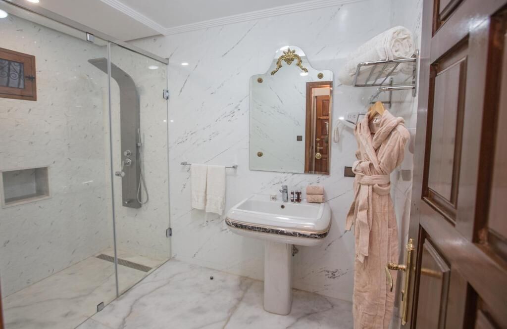 Une salle de bain dotée d’une douche à parois de verre, d’un lavabo sur colonne, d’un miroir avec un cadre orné et d’un porte-peignoir avec des serviettes.