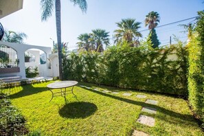 A well-maintained garden with a round table, a white building with arches, and palm trees. - RIAD SEBTI (Fès)