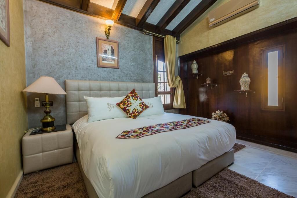 Quarto com uma cama grande, mesa de cabeceira, abajur, quadro na parede e porta de madeira.