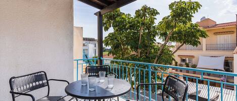 A balcony with a round table and four chairs, a view of buildings, and a tree.