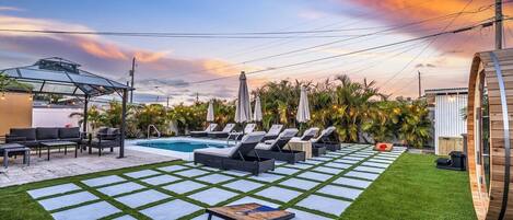 Un área de piscina con sillones de descanso, una mesa y una pérgola.