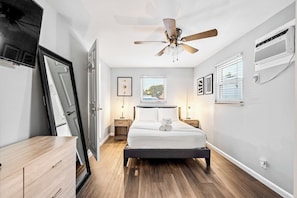 A bedroom with a bed, a ceiling fan, a window with blinds, a bedside table, and a nightstand. - 4BR Bio Hack Retreat: HTD Pool~Sauna~Hot Tub~Plunge (West Palm Beach)