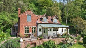 Une maison en briques avec un toit végétalisé, un jardin avec différentes espèces de plantes et du mobilier d’extérieur.