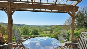 Une pergola en bois avec une table et des chaises en verre, donnant sur un paysage verdoyant.