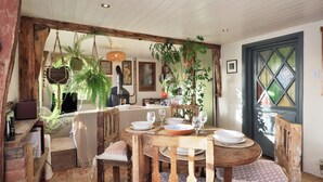 Un coin repas rustique, avec des meubles en bois, une table ronde dressée pour quatre personnes et des plantes suspendues.
