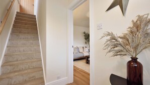 Eine Treppe führt zu einem Zimmer mit einem Bett, einer Vase mit Trockenpflanzen und einer sternförmigen Dekoration an der Wand.