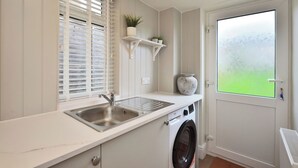 Eine kleine Küche mit Waschmaschine, Spüle und einem Fenster mit Jalousien.
