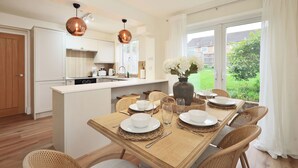 Eine moderne Küche mit weißen Schränken, eine Essecke mit einem Holztisch, gedeckt für vier Personen, und ein großes Fenster mit Blick auf Grünflächen.