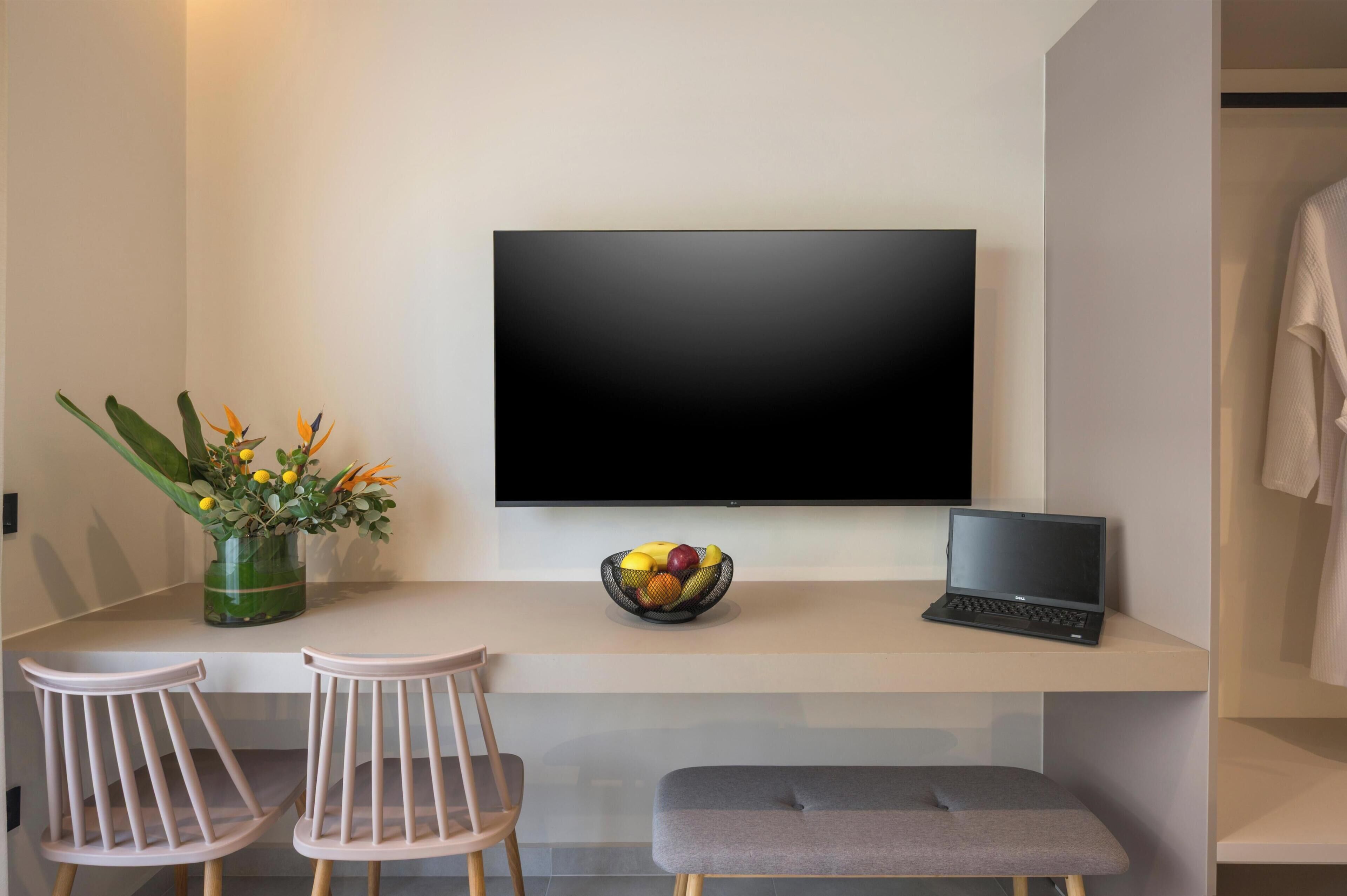 Una habitación moderna con una televisi ón de pantalla plana, una computadora portátil, un frutero y dos sillas.