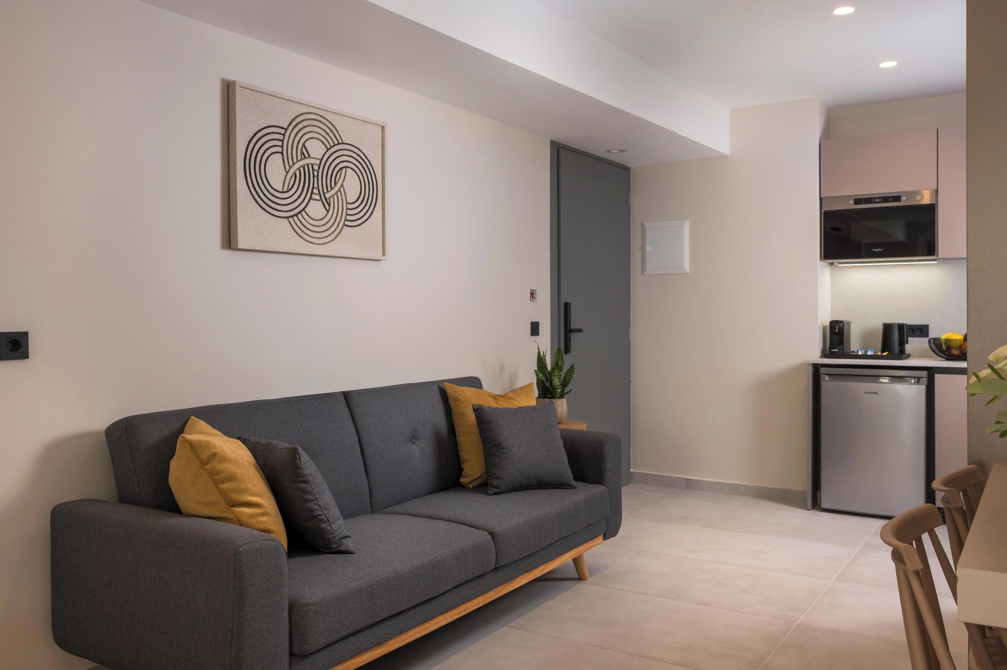 Una sala de estar moderna con un sofá gris, una obra de arte minimalista y una cocina con horno y lavavajillas integrados.