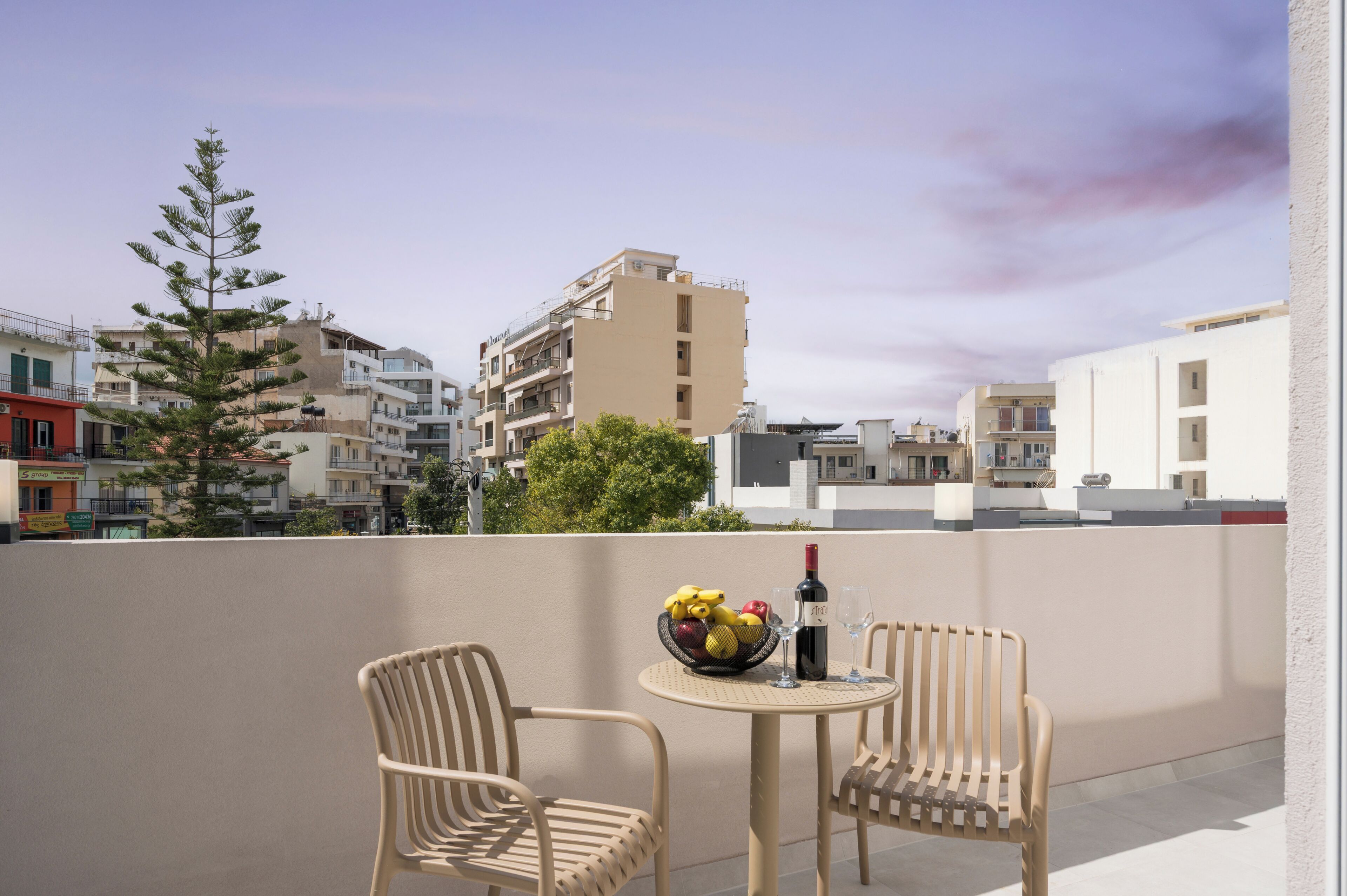 A balcony with two wicker chairs, a small round table, a bowl of fruit, a bottle of wine, and a glass.