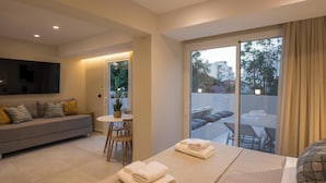 Ein modernes Hotelzimmer mit einer Couch, einem Esstisch, einem Balkon mit Sitzgelegenheit und einem großen Fenster.