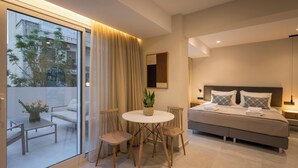 A modern bedroom with a bed, bedside tables, a small round table with chairs, and a view through a glass door. - Hermes City Living (Chania)