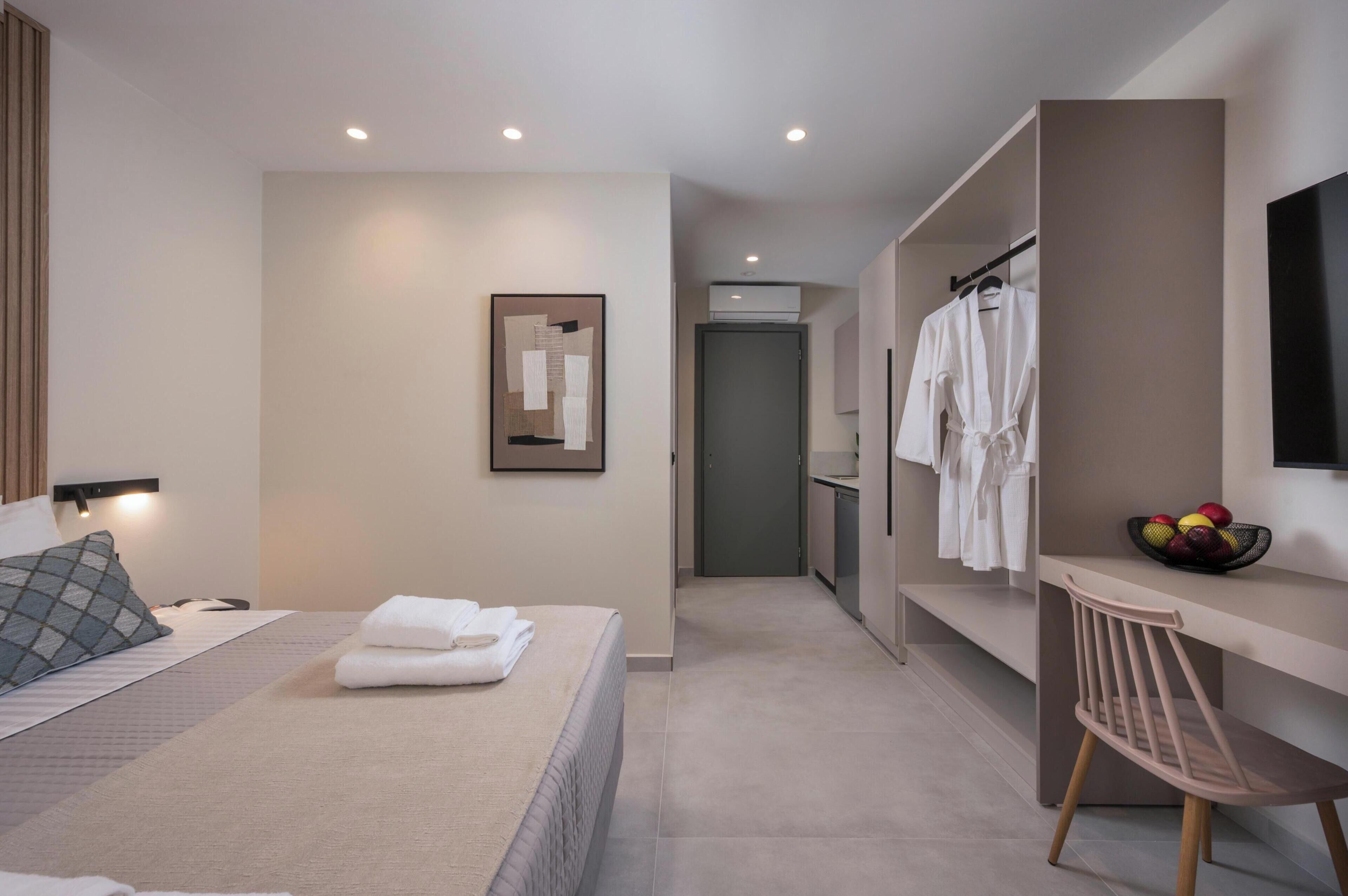 A hotel room with a bed, a desk, a chair, a mirror, and a wall-mounted TV.