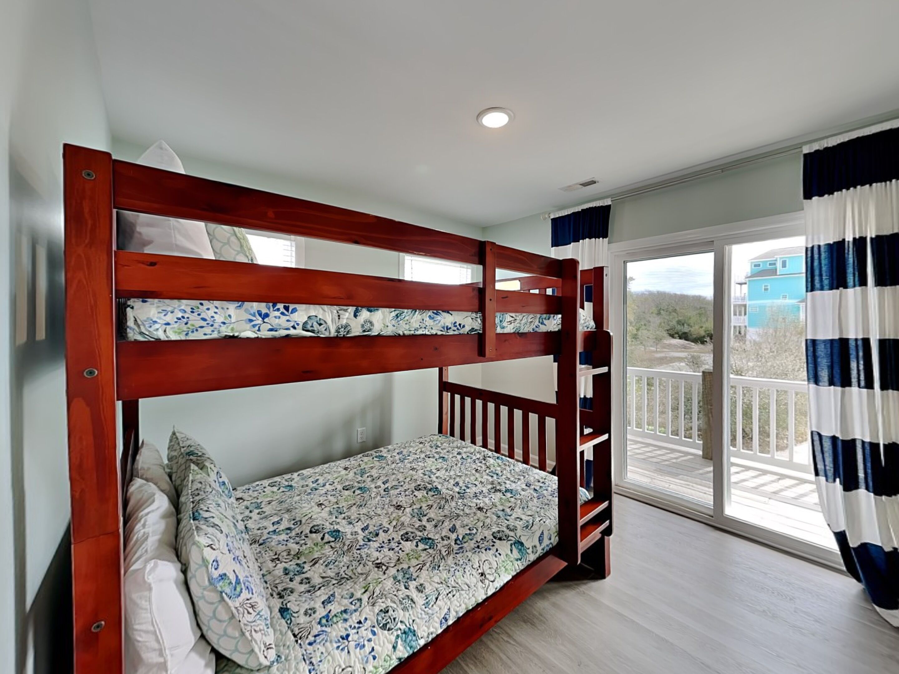 Una cama individual con ropa de cama floral, un balcón con vistas y una puerta corrediza de cristal.