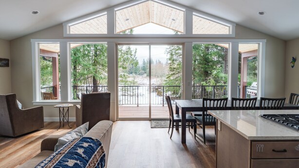 A modern kitchen with a large island, a dining area, and a cozy seating space with a view of trees. - May Creek Peaks: Custom built home on private acres w/ mountain views, covered spa, luxury amenities (Gold Bar)