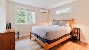 A bedroom with a wooden bed, a nightstand, a dresser, and a window with a view of trees. - May Creek Peaks: Custom built home on private acres w/ mountain views, covered spa, luxury amenities (Gold Bar)
