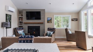 A living room with a fireplace, two sofas, a TV, and a window with a view of trees. - May Creek Peaks: Custom built home on private acres w/ mountain views, covered spa, luxury amenities (Gold Bar)