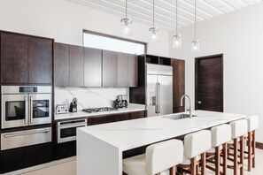 A modern kitchen with dark cabinets, stainless steel appliances, a marble countertop, and bar stools.