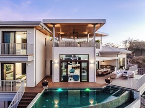 A modern two-story house with a pool, a balcony, and a dining area.