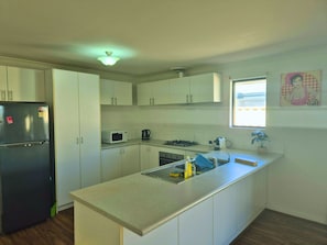 Een keuken met witte kastjes, een zwarte koelkast, een magnetron, een fornuis en een raam met uitzicht.