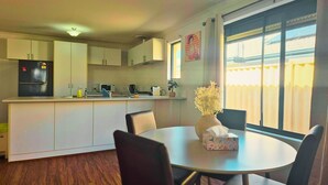 Cocina compacta equipada con refrigerador, microondas y cafetera. Hay una mesa de comedor con sillas y un florero con flores.