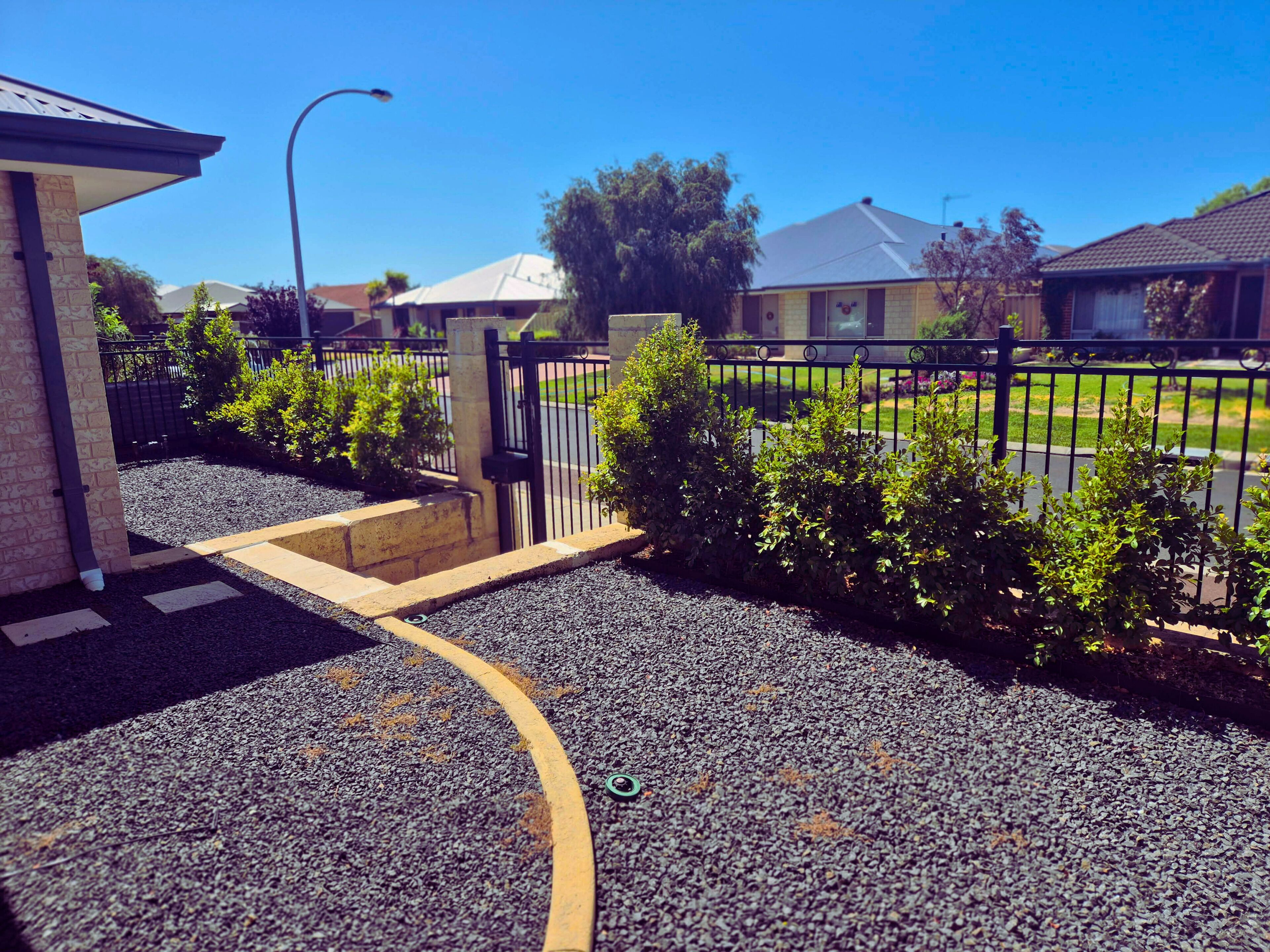 A residential area with a gated entrance, a paved driveway, and a street visible in the background.