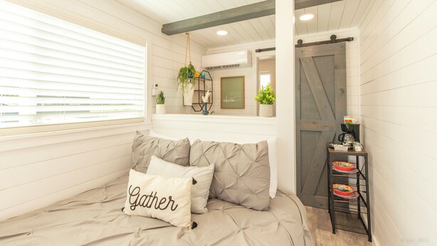 A room with a bed, a bedside table with a plant, a wall-mounted shelf, and a sliding barn-style door. - Scenic Canyon Lake Container Retreat (Canyon Lake)