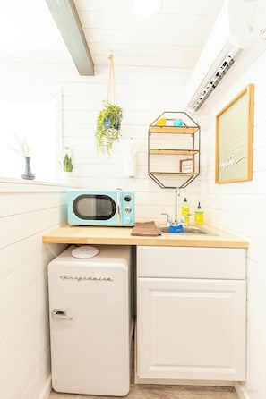 A compact kitchen with a microwave, a small refrigerator, a wooden countertop, a hanging plant, and a shelf with toiletries. - Scenic Canyon Lake Container Retreat (Canyon Lake)
